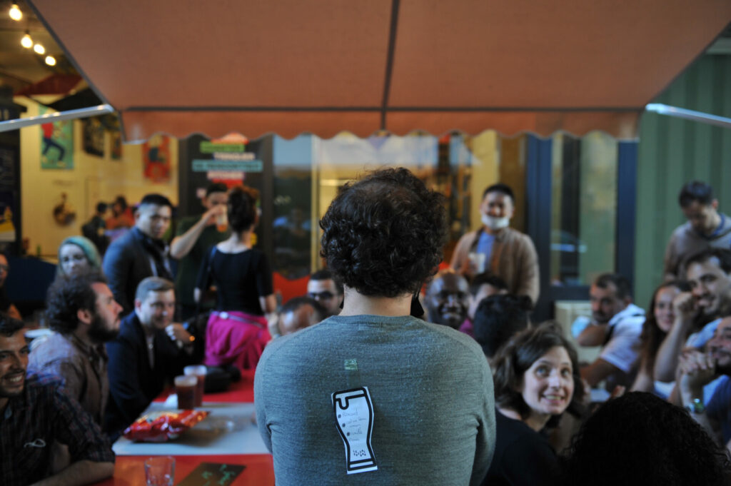 Un homme debout façe a une foule assise, fais rencontrer 2 tables pour sociabiliser